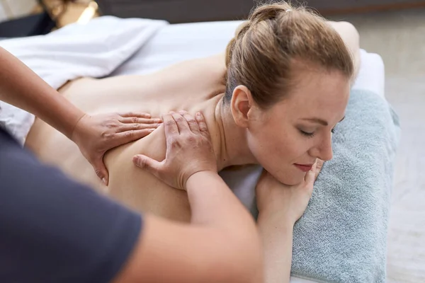 Chińska kobieta masażystka daje leczenie atrakcyjny blond klienta na stole do masażu w jasnym biurze medycznym — Zdjęcie stockowe
