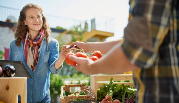 Vänlig kvinna tenderar en ekologisk vegetabiliska stall på en farmers market och säljer färska grönsaker från takträdgården — Stockfoto