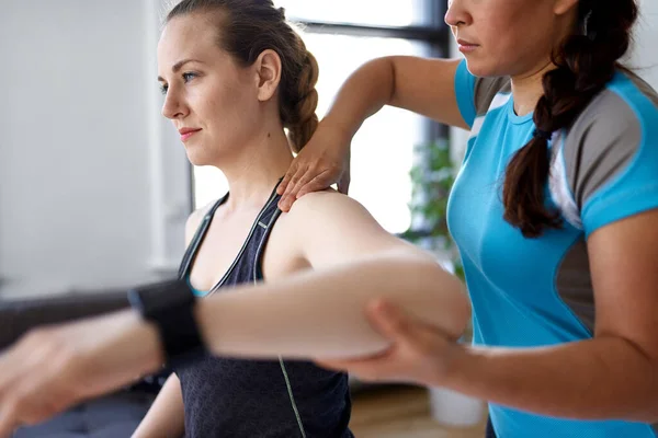 Chinesische Physiotherapeutin bei der Behandlung einer attraktiven blonden Kundin in einer hellen Arztpraxis — Stockfoto