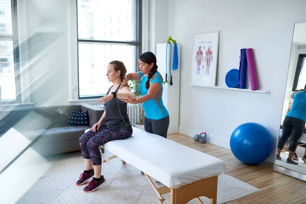 Chinese woman physiotherapy professional giving a treatment to an attractive blond client in a bright medical office — Stock Photo, Image