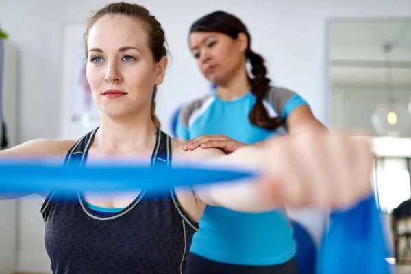 Kinesisk kvinna sjukgymnastik professionell ger en behandling med hjälp av elastiska MOTSTÅNDSBAND till en attraktiv blond klient i ett ljust medicinskt kontor — Stockfoto