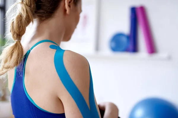 Mulher loira atraente em um escritório de terapia desportiva brilhante com fita cinesio em seu pescoço e ombro para curar a dor — Fotografia de Stock