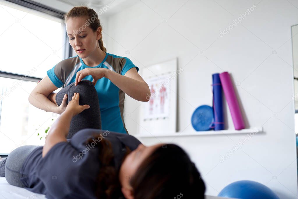 Caucasian woman physiotherapist strectching the leg and knee of a mid-adult chinese female patient sitting on a massage table