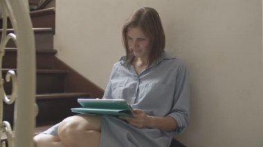 Yakın çekim genç esmer kadınlar ahşap merdivenlerde oturan ve tablet üzerinde çalışıyor. Klasik iç tablet ile konuşan kadın yetişkin