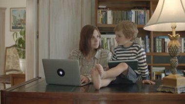 Sarışın yürümeye başlayan çocuk ahşap masada oturan tablet üzerinde oynayan çalışan anne rahatsız