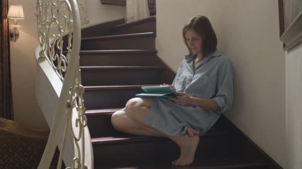 Jonge brunette vrouwen zittend op houten trap en werken op Tablet. Vrouwelijke volwassen praten per tablet in klassiek interieur — Stockvideo