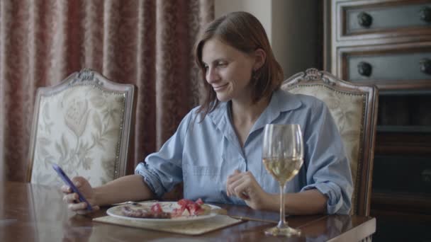 Брюнетка жінки, що мають їжу зі склом білого вина говорити по телефону — стокове відео