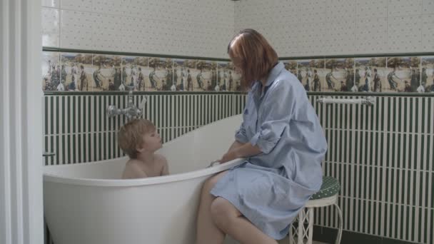 Junge brünette Mutter hilft ihrem kleinen Sohn, im klassischen Interieur zu baden — Stockvideo