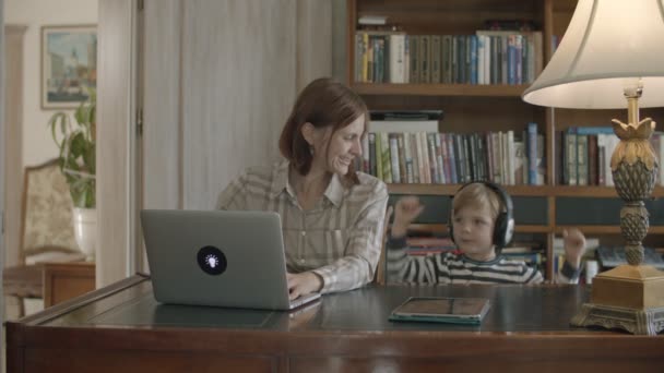 Брюнетка мати працює вдома з малюк сина прослуховування музики в навушниках — стокове відео