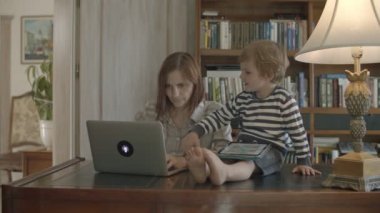 Sarışın yürümeye başlayan çocuk ahşap masada oturan tablet üzerinde oynayan çalışan anne rahatsız