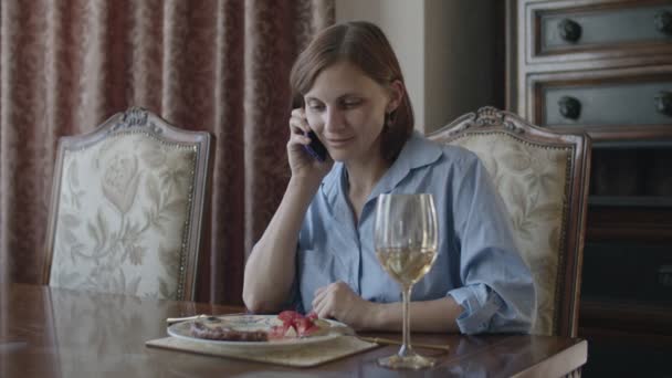 Брюнетка жінки, що мають їжу зі склом білого вина і говорити по телефону — стокове відео