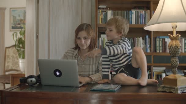 Brunette moeder werkt thuis met peuter zoon het luisteren van de muziek in een koptelefoon — Stockvideo
