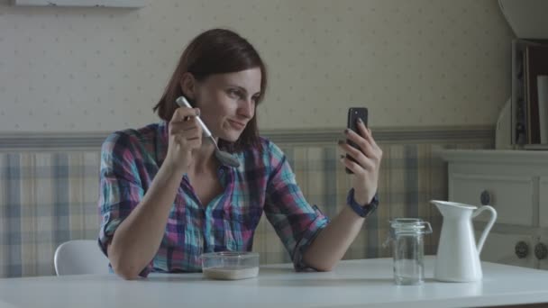 Молоді жінки розмовляють онлайн і їдять безглютенові кукурудзяні пластівці з веганським молоком зі смартфоном — стокове відео