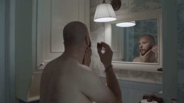Віддзеркалення у дзеркалі голими головами 30-х чоловік піклується про свою бороду у ванній кімнаті Провансу. Молодий чоловік наносить олію бороди після душу . — стокове відео