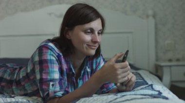 Çekici genç kadın yatakta yatan ve akıllı telefon ve dizüstü bilgisayar üzerinden online sörf 