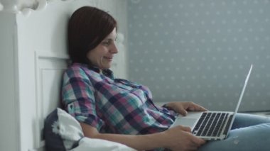 Çekici genç kadın yatakta yatan ve akıllı telefon ve dizüstü bilgisayar üzerinden online sörf 