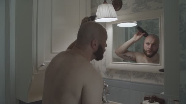 Reflectie in de spiegel van de jonge man scheren hoofd en baard in de Provence badkamer — Stockvideo