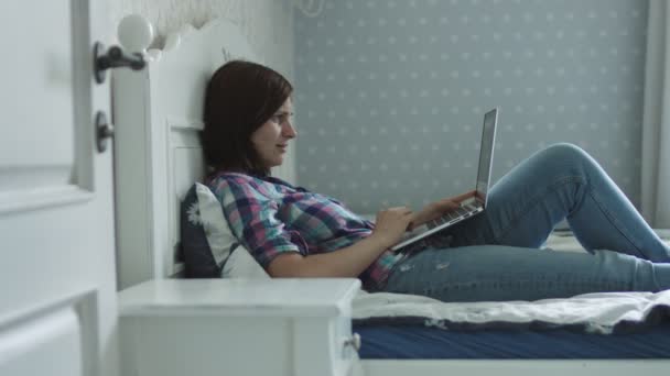 매력적인 젊은 여성은 침대에 누워 스마트 폰과 노트북을 통해 온라인으로 서핑 — 비디오
