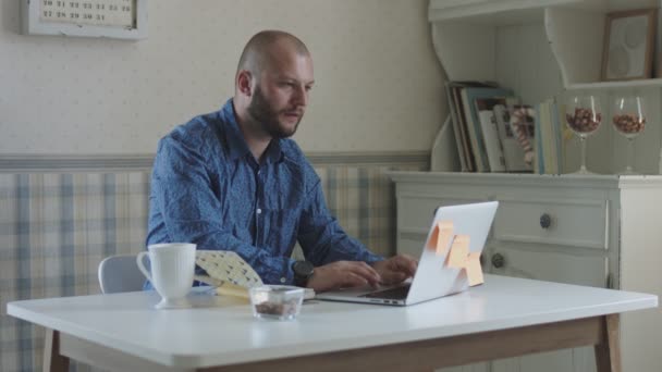 Genç erkek serbest dizüstü bilgisayar ve akıllı telefon çay ve aperatifler ile masada oturan çalışan — Stok video