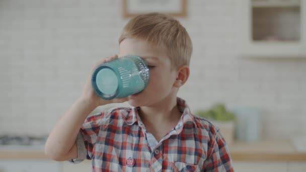 Kleinkind isst Schokokekse und trinkt Joghurt, sitzt allein in Zeitlupe auf heller Küche — Stockvideo