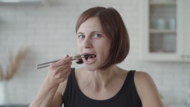 Mujer morena joven comiendo sushi en la cocina luminosa. Europea hembra comer japonés comida . — Vídeo de stock