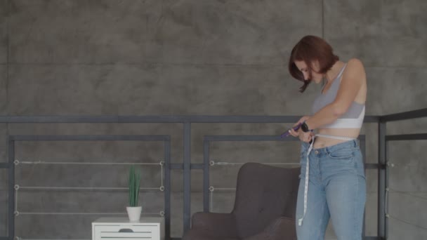 Jonge vrouw het resultaat van gewichtsverlies bewonderen terwijl het dragen van oude jeans in de slaapkamer. Gelukkige vrouw het nemen van foto van haar buik nadat je verloren gewicht. — Stockvideo