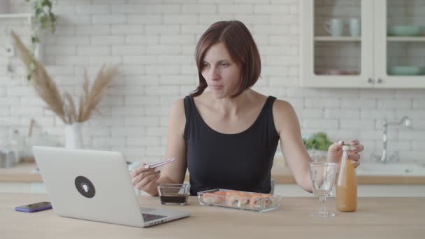 Jeune femme brune mangeant des sushis sur une cuisine lumineuse. Européen femelle manger japonais nourriture . — Video