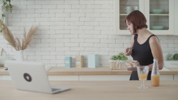 Mujer morena joven caminando y comiendo sushi en la cocina luminosa. Europea mujer comiendo comida japonesa y hablando por teléfono — Vídeos de Stock