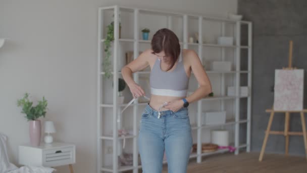 Jovem admirando o resultado da perda de peso ao usar jeans velhos no quarto. Mulher feliz tirando foto de sua barriga depois que você perdeu peso . — Vídeo de Stock