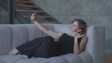 Pretty genç kadınlar rahat kanepede oturan akıllı telefon sohbet ile mutlu. Cep telefonu selfie yapma siyah elbiseli çekici kadın