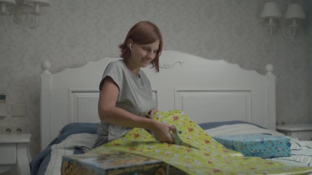 Slow motion of young pretty women wrapping birthday gifts for kids sitting in provence bedroom. Mother preparing presents for kids birthday. — Stock Video