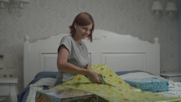 Mouvement lent des jeunes jolies femmes enveloppant des cadeaux d'anniversaire pour les enfants assis dans la chambre à coucher de provence. Mère préparant des cadeaux pour les enfants anniversaire . — Video