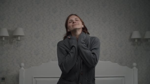 Movimiento lento de mujeres jóvenes y bonitas con auriculares inalámbricos bailando en la cama vestida con chaqueta de hombre. Bailando en habitación blanca provence — Vídeos de Stock