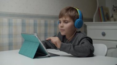 Autistic boy learning online with tablet computer and headphones in slow motion. Kid with autism happy to use gadget. Autism awareness 
