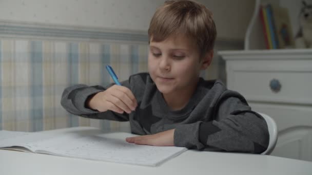 Niño autista practicando con la escritura sentado en la mesa en cámara lenta. Niño con autismo escribiendo con pluma . — Vídeos de Stock