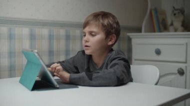 Autistic boy learning online with tablet computer and headphones in slow motion. Kid with autism happy to use gadget. Autism awareness 