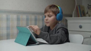Autistic boy learning online with tablet computer and headphones in slow motion. Kid with autism happy to use gadget. Autism awareness 