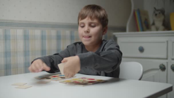 Autistic kid completing puzzle on the table in slow motion. Child with autism sorting cards. Autism awareness — Stock Video