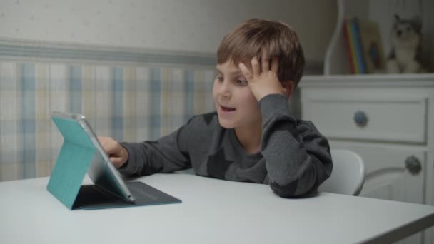 Autystyczny chłopiec uczący się online z tabletem i słuchawkami w zwolnionym tempie. Dzieciak z autyzmem chętnie użyje gadżetu. Świadomość autyzmu — Wideo stockowe
