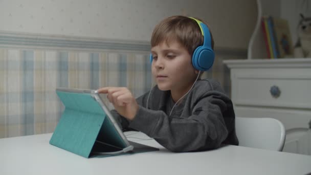 自闭症男孩通过平板电脑和耳机慢动作在网上学习。 孤独症患儿很乐意使用小工具。 自闭症意识 — 图库视频影像