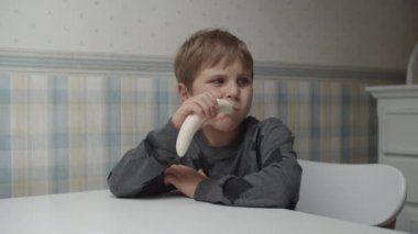 Autistic kid eating a banana in slow motion sitting at the table. Boy is happy with the food. Autism awareness 