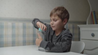 Autistic kid opening bottle with water in slow motion sitting at the table. Boy is happy with drinking water. Autism awareness 