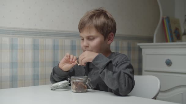 Аутистичный ребенок ест здоровые закуски в замедленной съемке, сидя за столом. Мальчик доволен едой. Осознание аутизма — стоковое видео