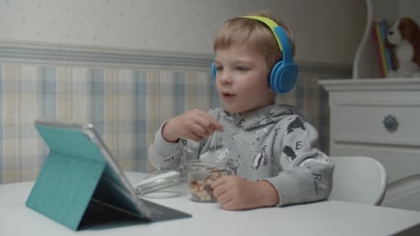 Niño rubio feliz con auriculares comiendo bocadillos saludables, cantando canciones y bailando con las manos en cámara lenta . — Vídeos de Stock