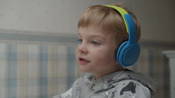 Primer plano del chico rubio en auriculares comiendo bocadillos saludables, cantando canciones y bailando con las manos en cámara lenta . — Vídeo de stock