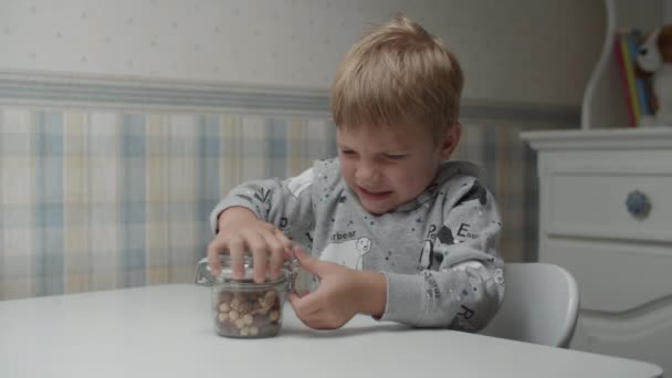 Blond pojke försöker öppna locket på en burk för att äta hälsosamma mellanmål. Ungen lyckades öppna flaskan med mat. — Stockvideo