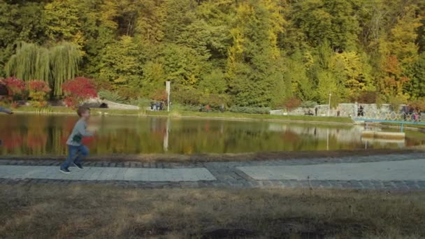 Dos hermanos corriendo en el hermoso parque de otoño junto al lago en cámara lenta. Chicos jugando y corriendo en Fall Park. Dispara con steadicam . — Vídeo de stock