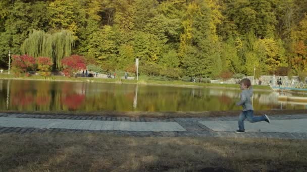 Dos hermanos corriendo en el hermoso parque de otoño junto al lago en cámara lenta. Chicos jugando y corriendo en Fall Park. Dispara con steadicam . — Vídeo de stock