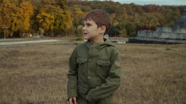 Chłopiec stojący i rozglądający się po jesiennym polu z betonową strukturą na tle. Chłopiec zaczyna biegać w jesiennym parku. Strzelaj w zwolnionym tempie, Steadicam. — Wideo stockowe