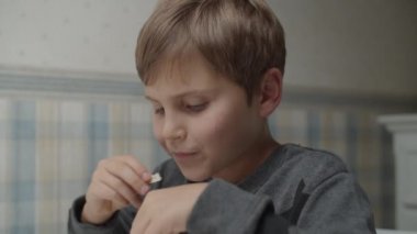 Otistik çocuk ağır çekimde sağlıklı atıştırmalıklar yiyor masada oturuyor. Çocuk yiyecekten memnun. Otizm farkındalığı 